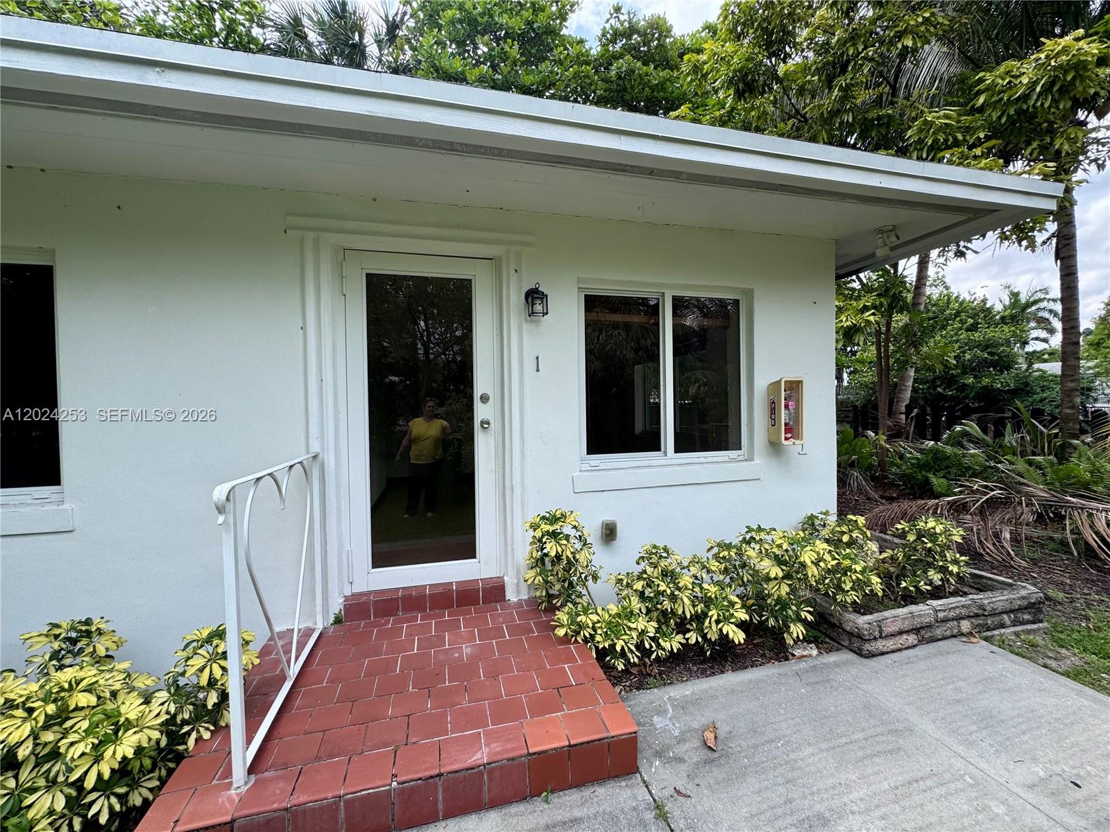 The exterior of a white building features a red-tiled entrance, a glass door, and landscaping — 8440 NE 1st Ave # 1, Miami FL 33138, MIAMI, FL