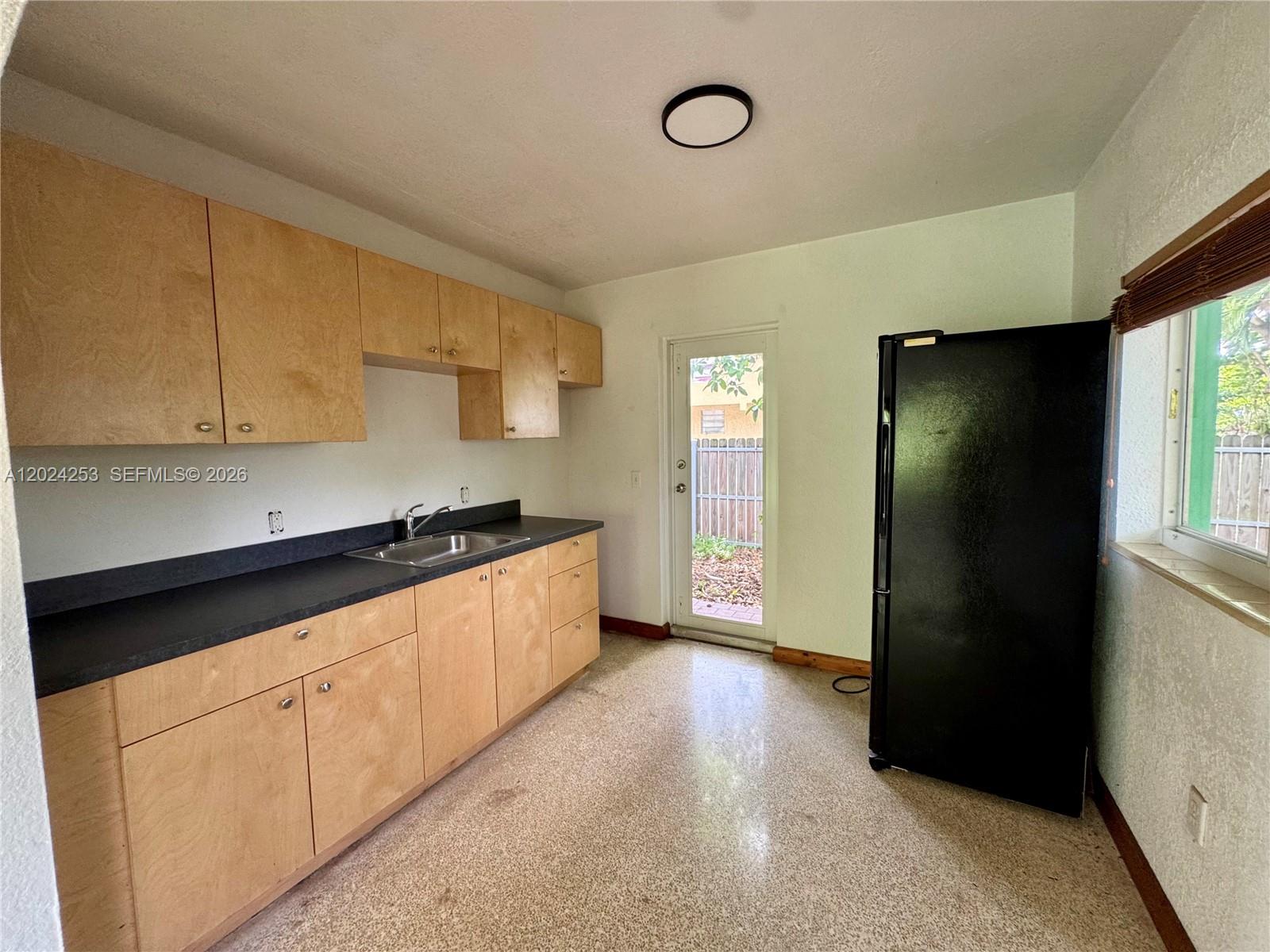 A kitchen features light wood cabinets, black countertops, a black refrigerator, and terrazzo flooring — 8440 NE 1st Ave # 1, Miami FL 33138, MIAMI, FL