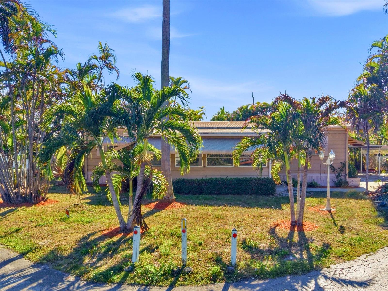 A single-story house with tan siding and metal awnings sits behind palm trees and lawn — 8903 Oak Street, Boynton Beach FL 33436, BOYNTON BEACH, FL