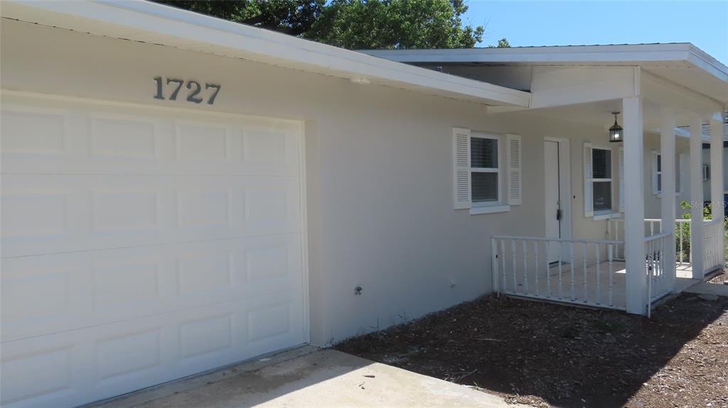 A white house exterior features a garage, a covered front porch, and a small lawn — 1727 THAMES STREET, CLEARWATER, FL