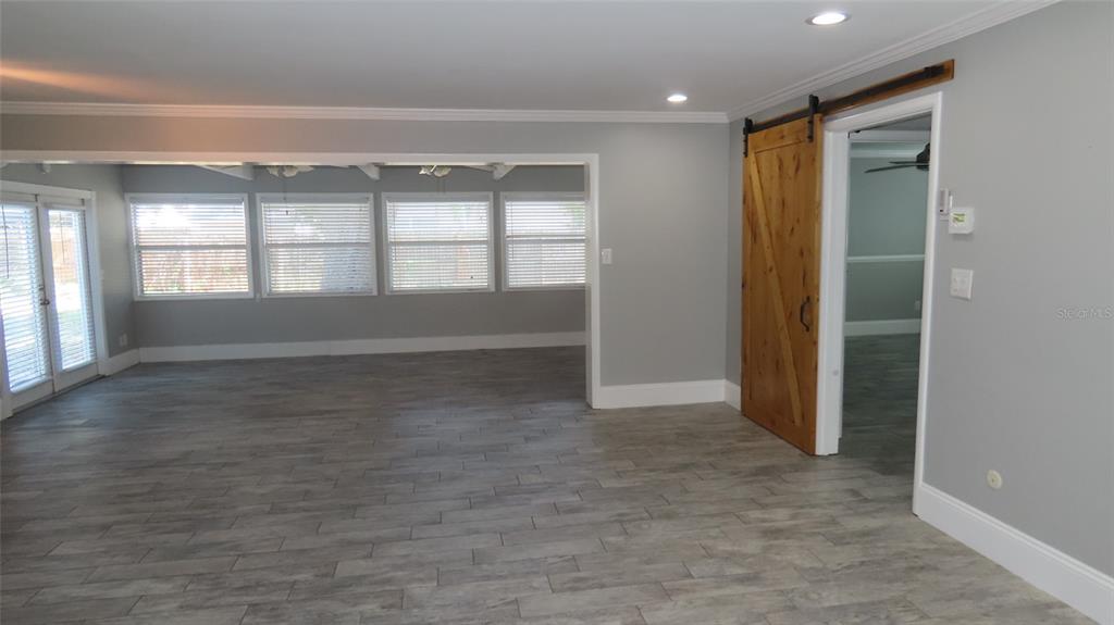 A room with gray wood-look tile flooring, a sliding barn door, and large windows — 1727 THAMES STREET, CLEARWATER, FL