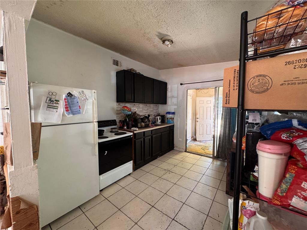 A kitchen features black cabinets, a white refrigerator, a white stove, and light-colored floor tiles — 1033 COLUMBIA STREET, ORLANDO, FL