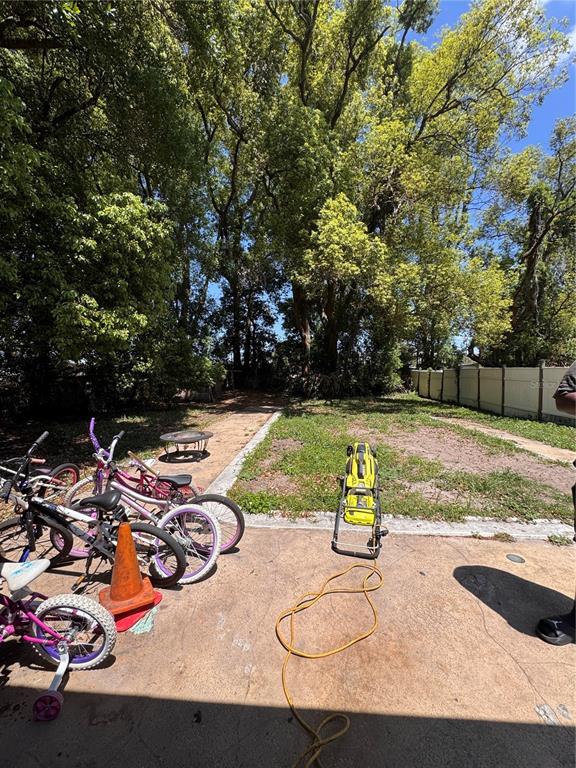 A backyard features a concrete patio with several bicycles, a pressure washer, and mature trees — 1033 COLUMBIA STREET, ORLANDO, FL