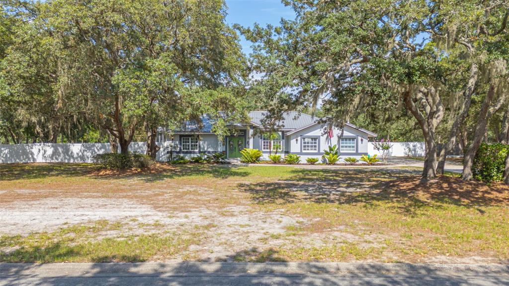 A single-story house with a metal roof sits behind a large yard with mature trees — 361 LAKE LENELLE DRIVE, CHULUOTA, FL