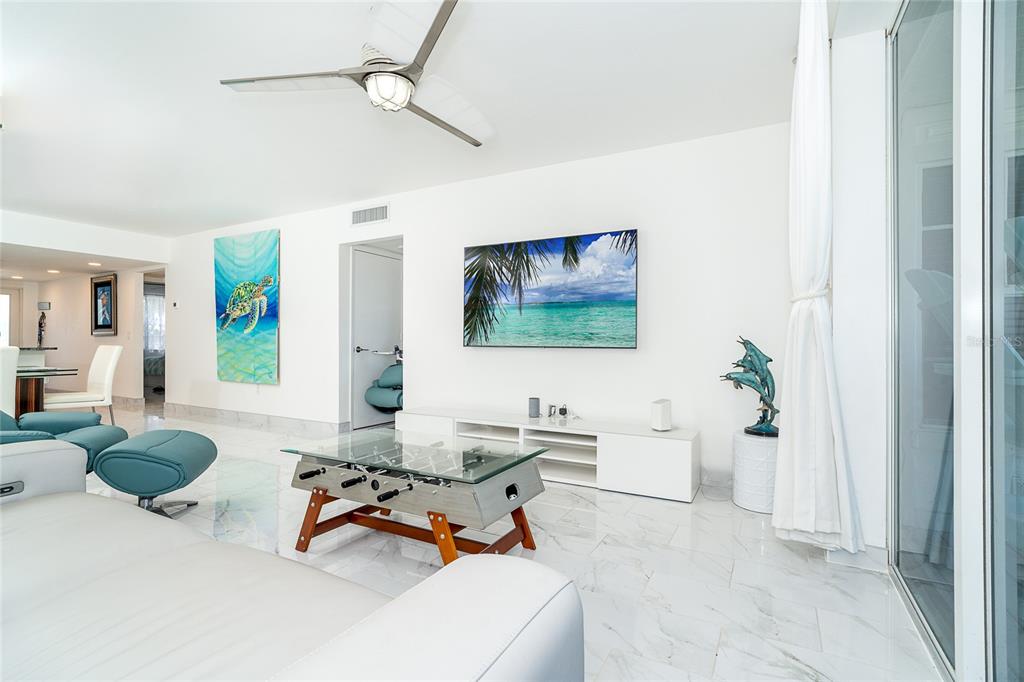 A bright living room features white marble floors, a foosball coffee table, and a wall-mounted television — 7500 PALM ISLAND DRIVE S UNIT 2111, PLACIDA, FL