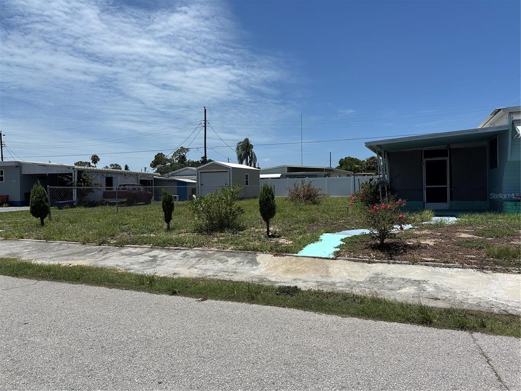 A grassy yard features a small shed, a chain-link fence, and a house with a porch — 2025 SHADY COVE DRIVE, HOLIDAY, FL