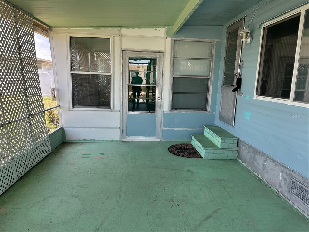A covered porch features green painted flooring, light blue siding, and a screen door — 2025 SHADY COVE DRIVE, HOLIDAY, FL