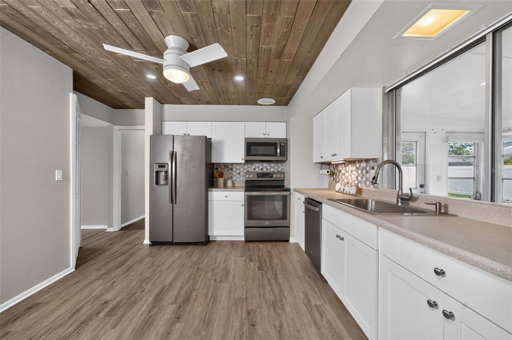 A kitchen features white cabinets, stainless steel appliances, a wood-plank ceiling, and light wood flooring — 559 MOUNT VERNON DRIVE, VENICE, FL