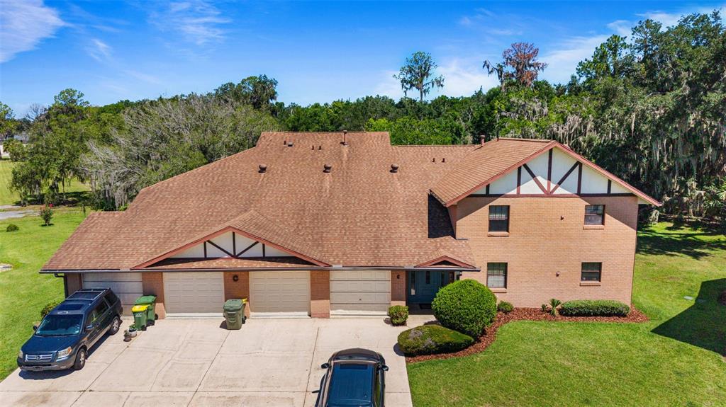 An aerial view of a two-story brick house with a multi-car garage and driveway — 100 E OAK TERRACE DRIVE UNIT C1, LEESBURG, FL
