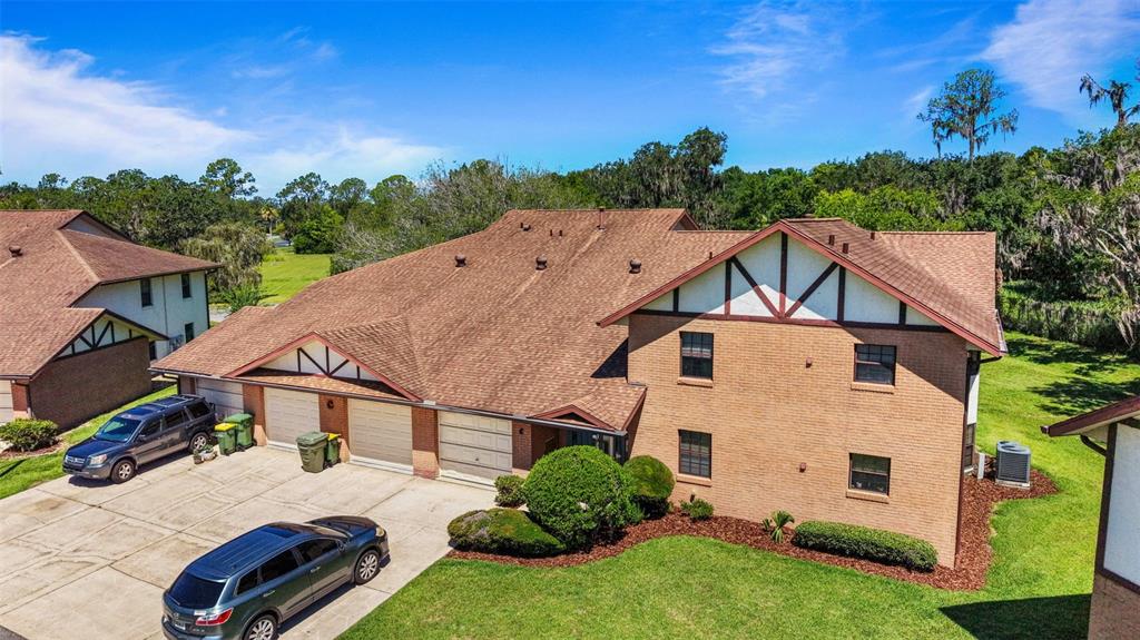 An aerial view of a two-story brick townhouse with a brown shingled roof and garages — 100 E OAK TERRACE DRIVE UNIT C1, LEESBURG, FL