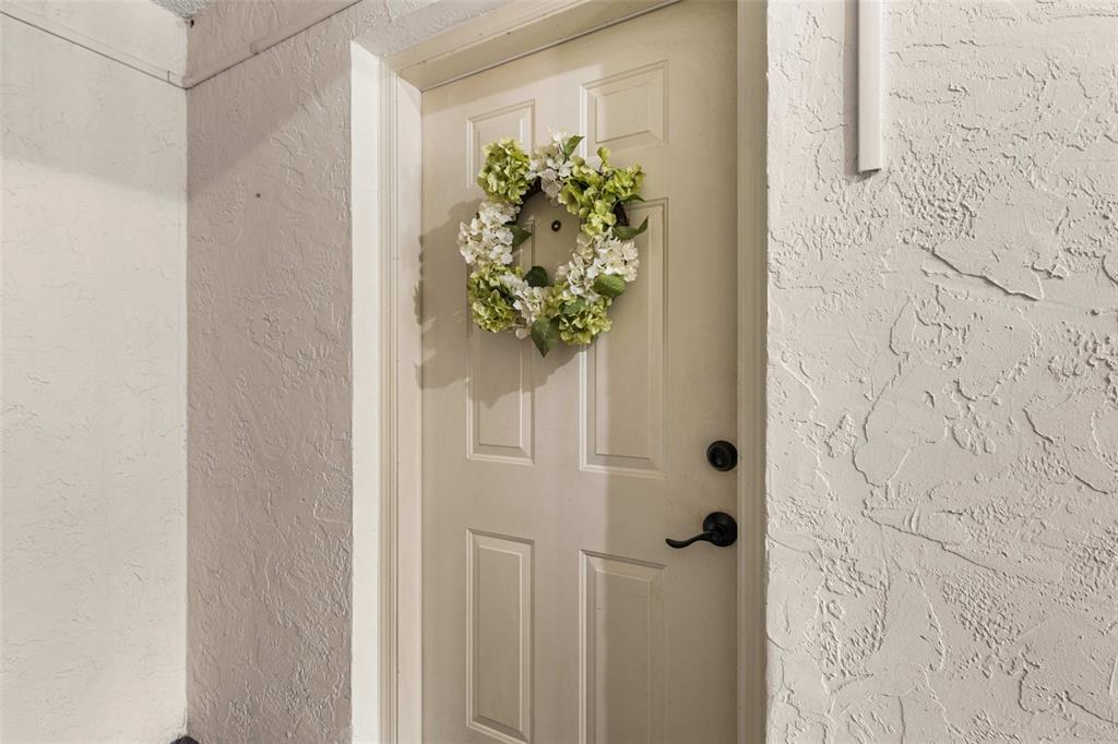 A beige front door with a floral wreath is set into a textured stucco wall — 100 E OAK TERRACE DRIVE UNIT C1, LEESBURG, FL