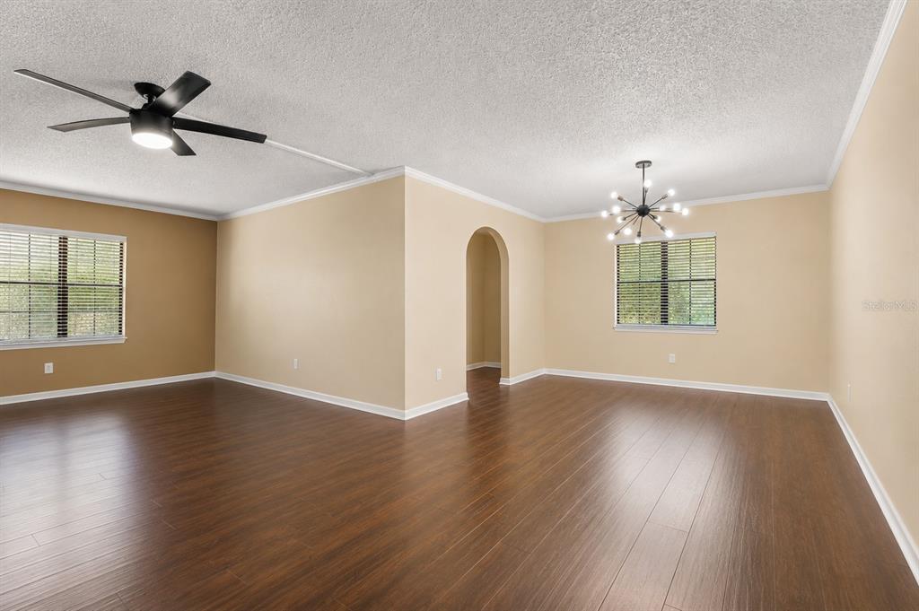 An empty living room features dark wood-look flooring, beige walls, a ceiling fan, and chandelier — 100 E OAK TERRACE DRIVE UNIT C1, LEESBURG, FL