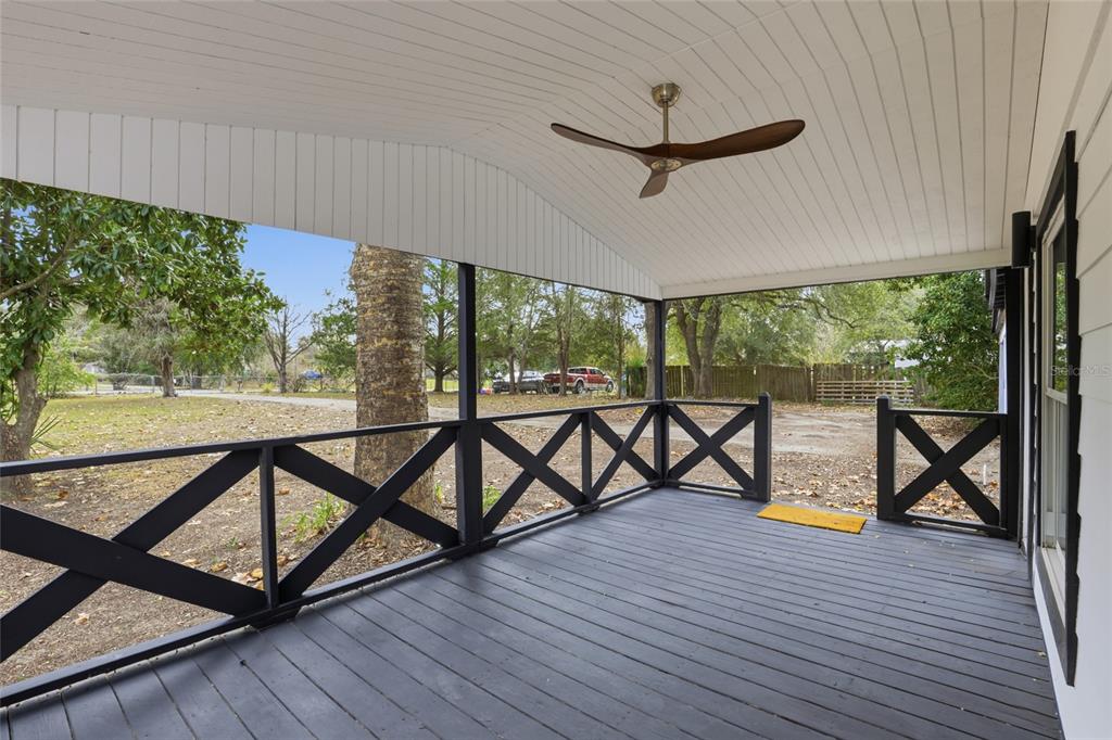 A covered porch with a dark wood deck, black X-pattern railings, and a ceiling fan — 9024 SW 104TH TERRACE, GAINESVILLE, FL