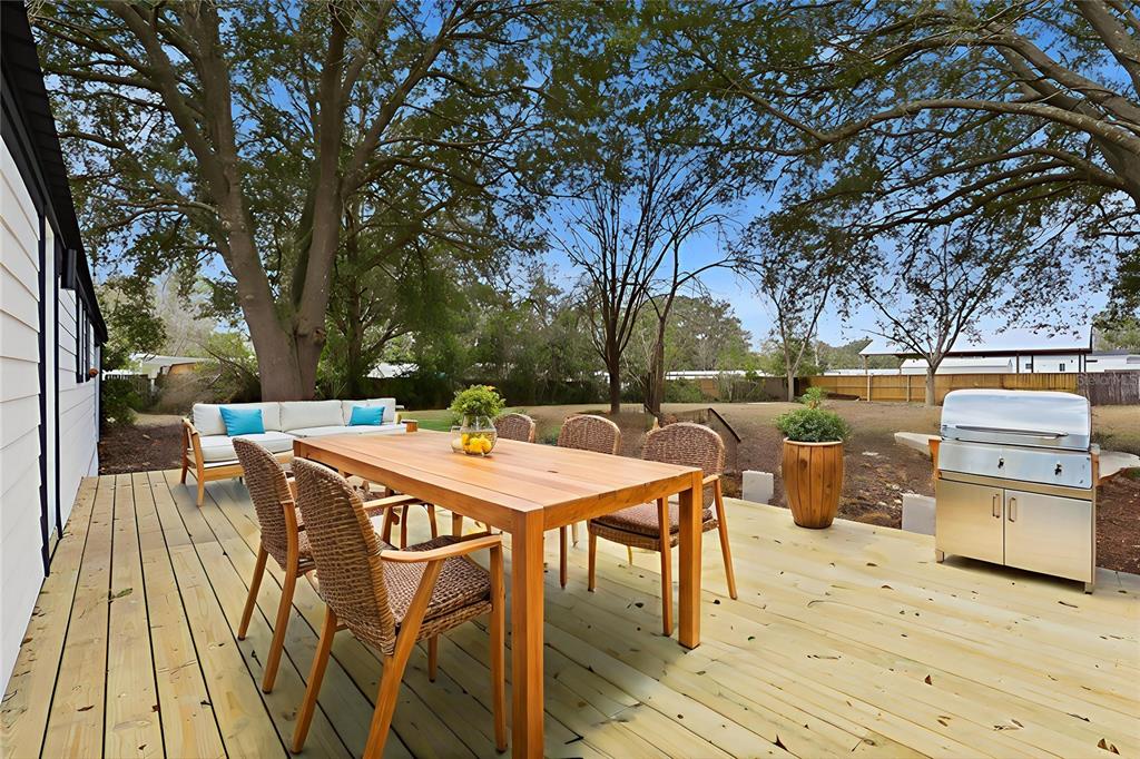 A wooden deck features a dining table, wicker chairs, a sofa, and a stainless steel grill — 9024 SW 104TH TERRACE, GAINESVILLE, FL