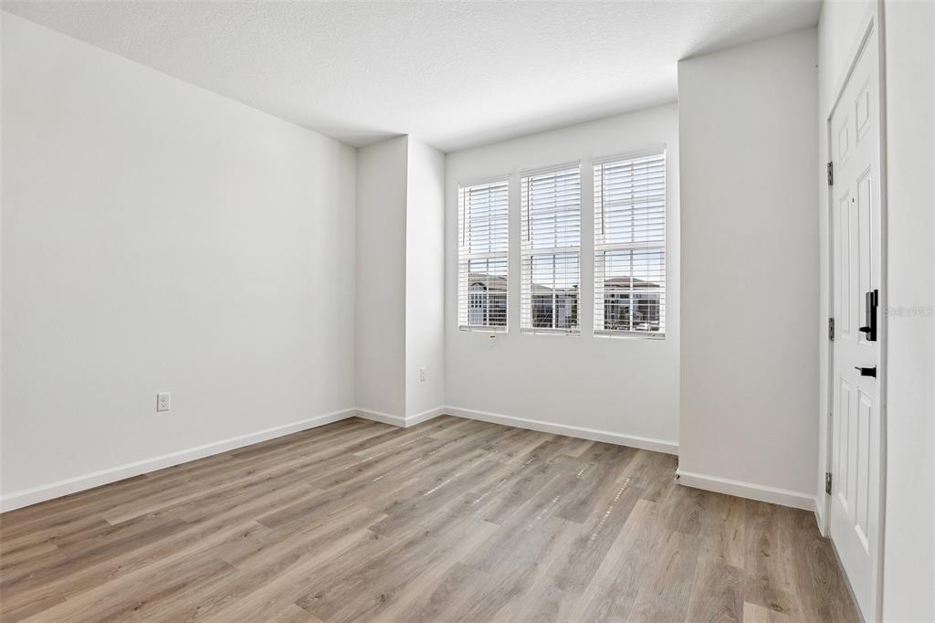 An empty room with white walls, wood-look flooring, and three windows with white blinds — 3075 SOLDIER CITY WAY UNIT 203, ST CLOUD, FL