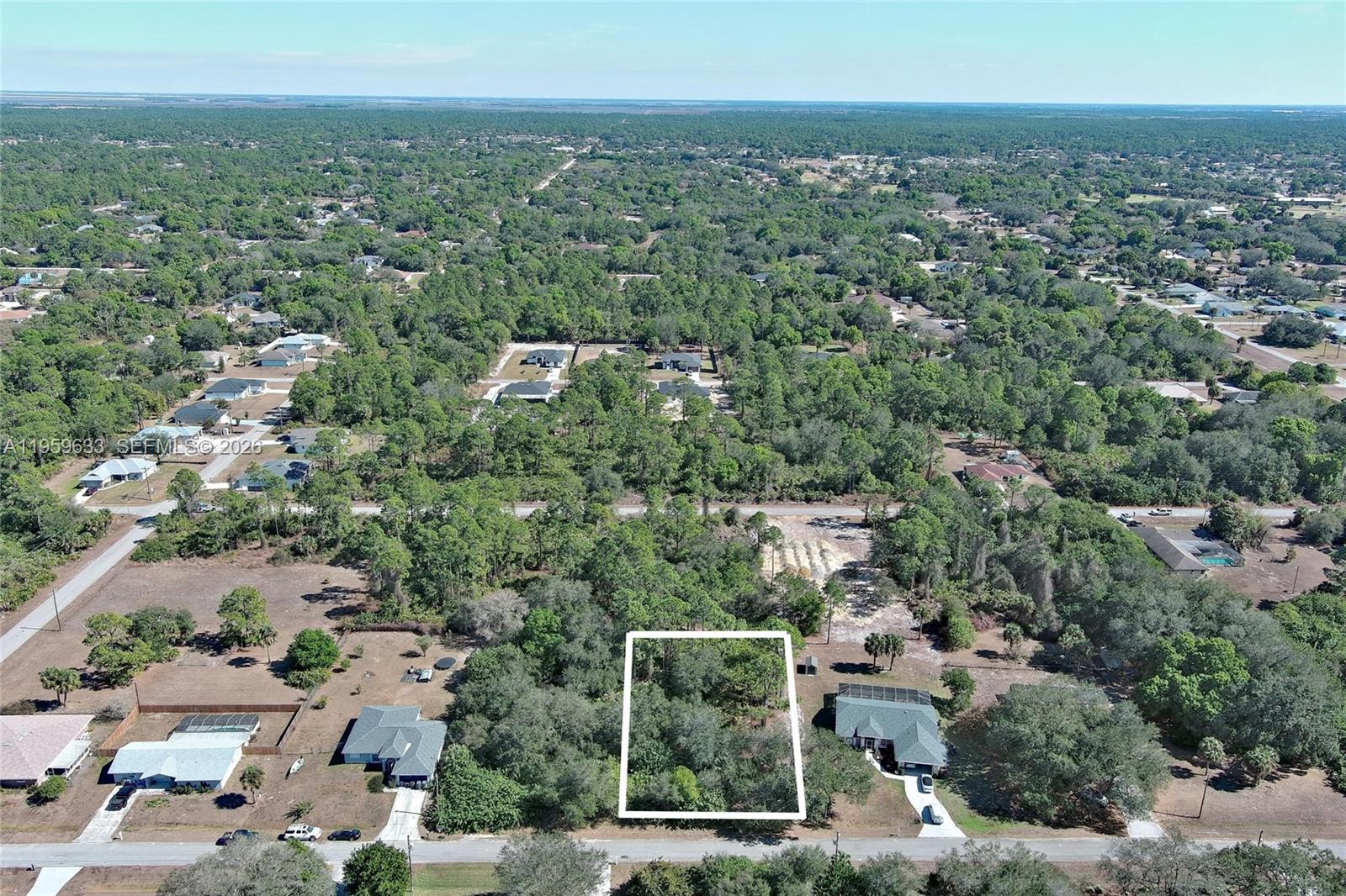 An aerial view shows a vacant, wooded residential lot outlined in white between two houses — 414 Lake Ave, Lehigh Acres FL 33972, LEHIGH ACRES, FL