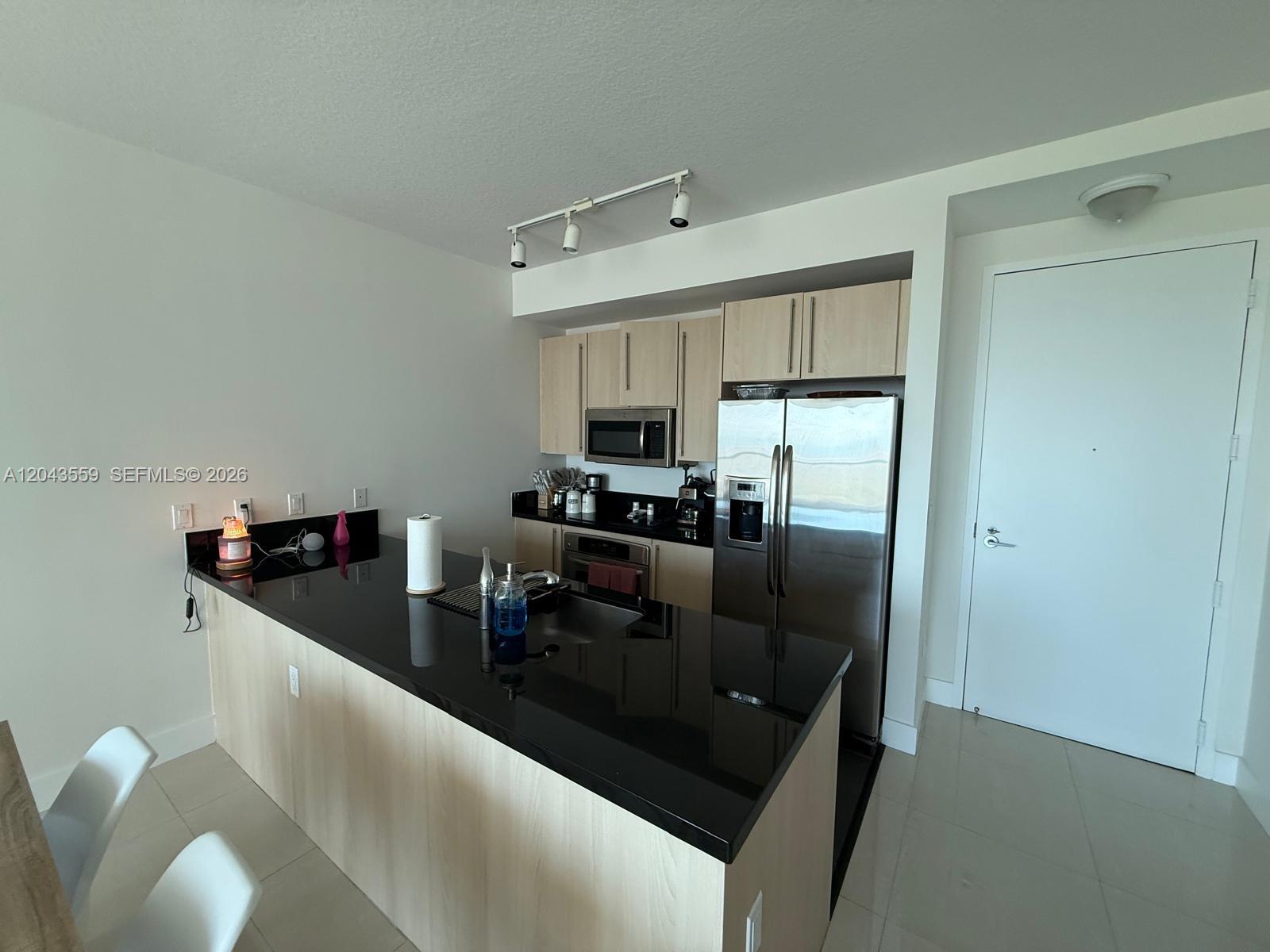 A kitchen features light wood cabinets, black countertops, stainless steel appliances, and a breakfast bar — 79 SW 12th St, Miami FL 33130, MIAMI, FL
