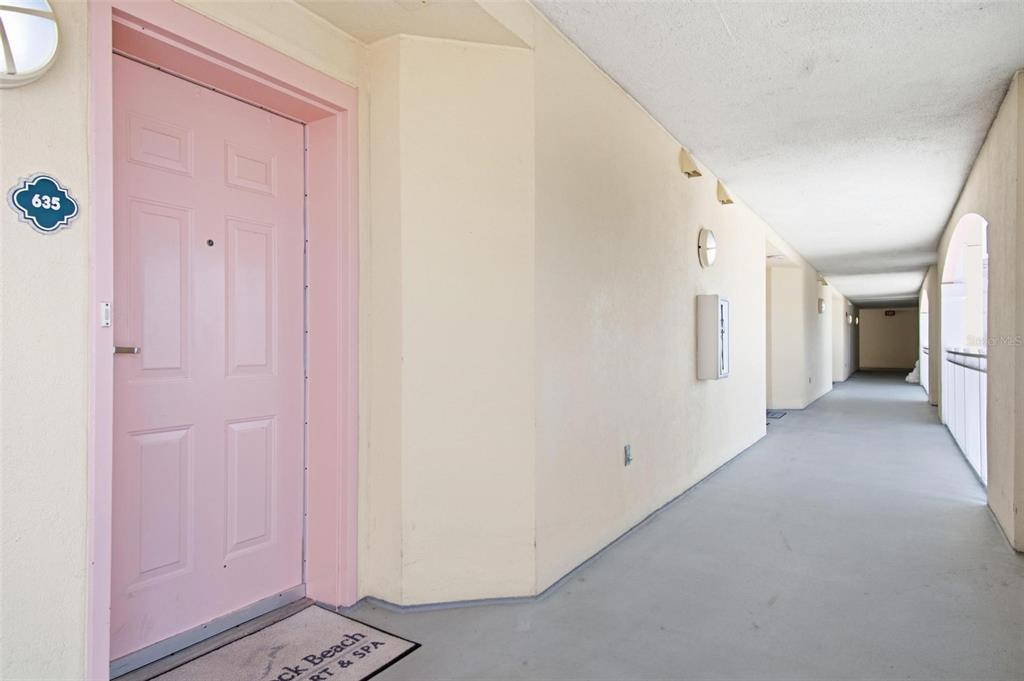 A pink door labeled 635 opens onto a long, covered outdoor hallway with beige walls — 200 OCEAN CREST DRIVE UNIT 635, PALM COAST, FL