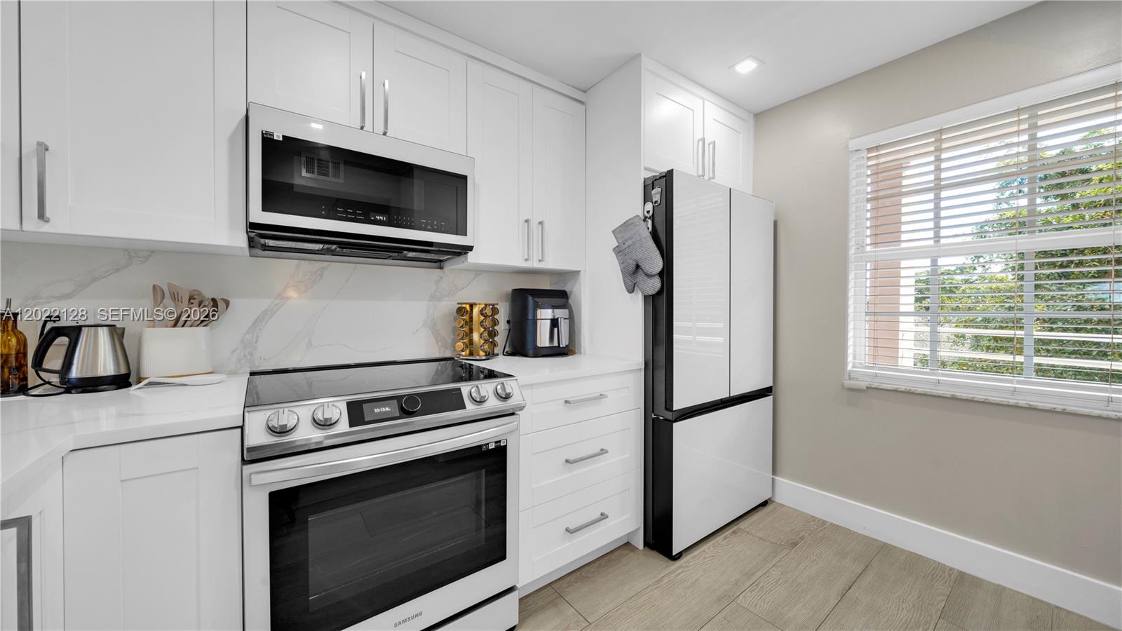 A modern kitchen features white cabinetry, stainless steel appliances, and a marble-patterned backsplash — 605 Oaks Dr # 502, Pompano Beach FL 33069, POMPANO BEACH, FL
