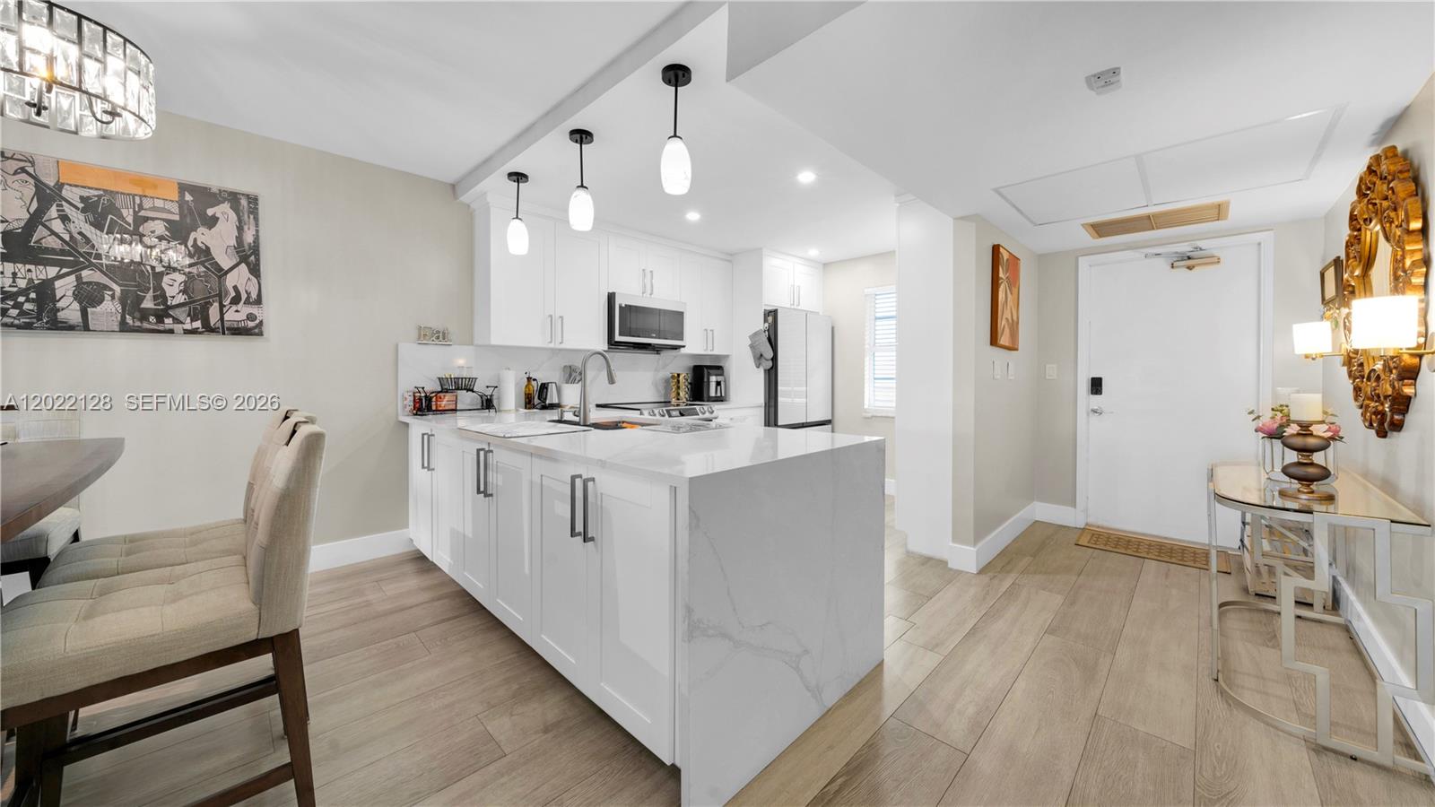 A modern kitchen features white cabinetry, a quartz waterfall island, and light wood flooring — 605 Oaks Dr # 502, Pompano Beach FL 33069, POMPANO BEACH, FL