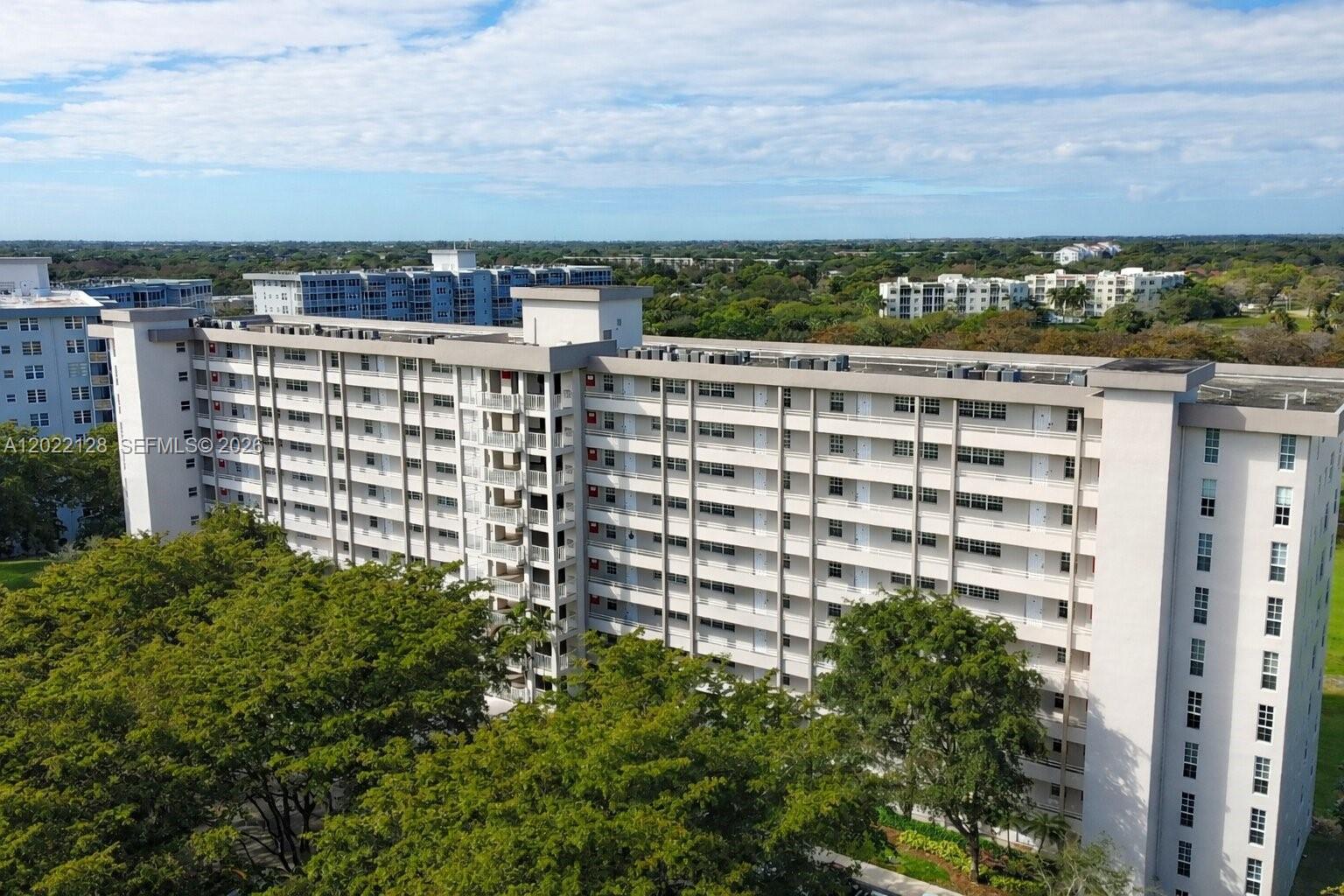 An aerial view shows a large, multi-story residential apartment building surrounded by trees — 605 Oaks Dr # 502, Pompano Beach FL 33069, POMPANO BEACH, FL