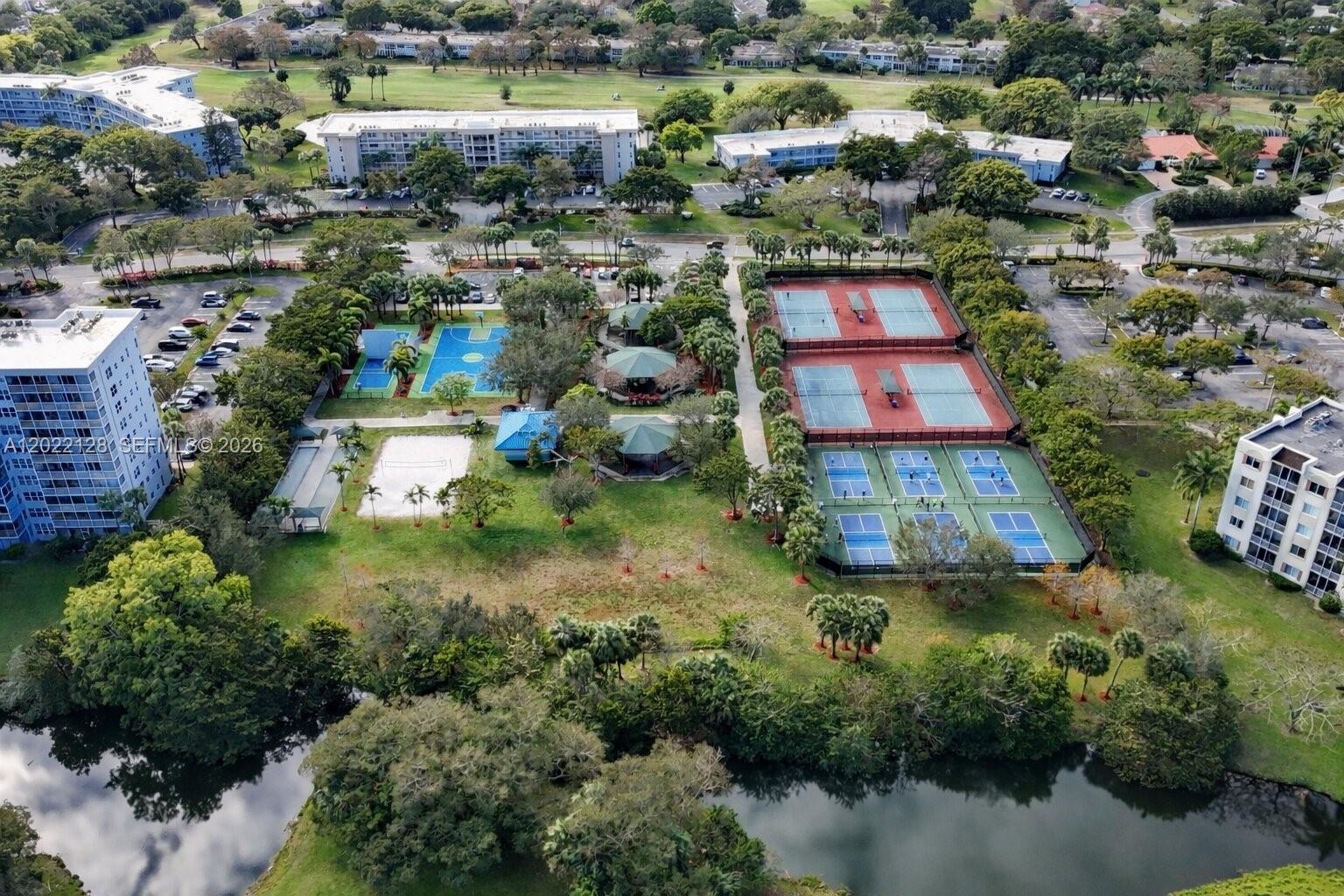 An aerial view shows tennis and pickleball courts, a volleyball court, and surrounding residential buildings — 605 Oaks Dr # 502, Pompano Beach FL 33069, POMPANO BEACH, FL