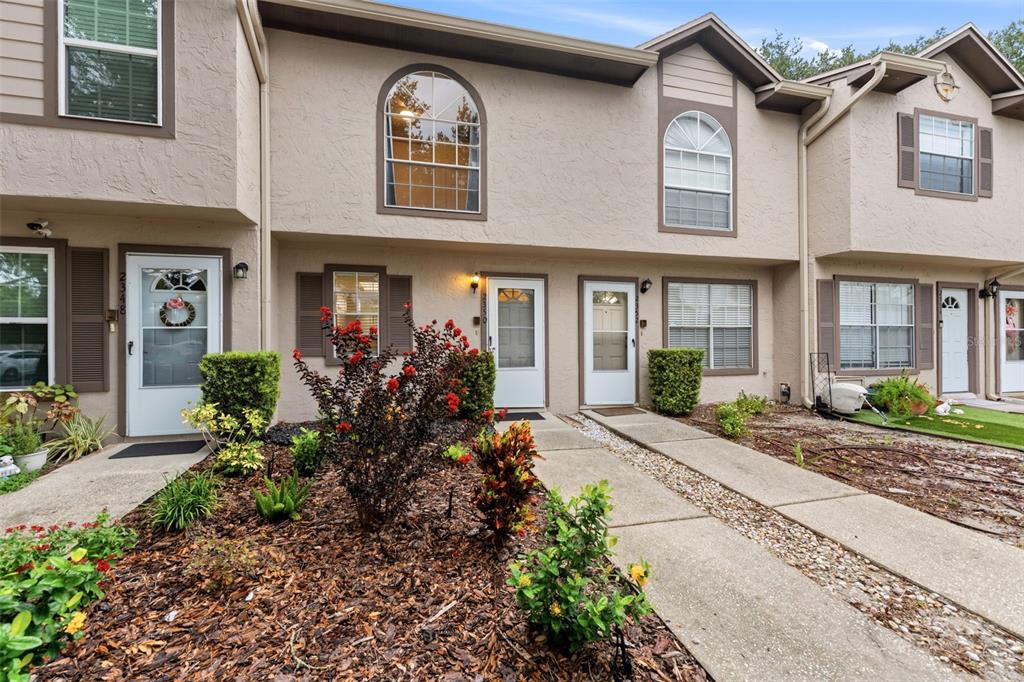 A row of multi-story townhouses features beige stucco siding, arched windows, and small front gardens — 2350 FLETCHERS POINT CIRCLE, TAMPA, FL