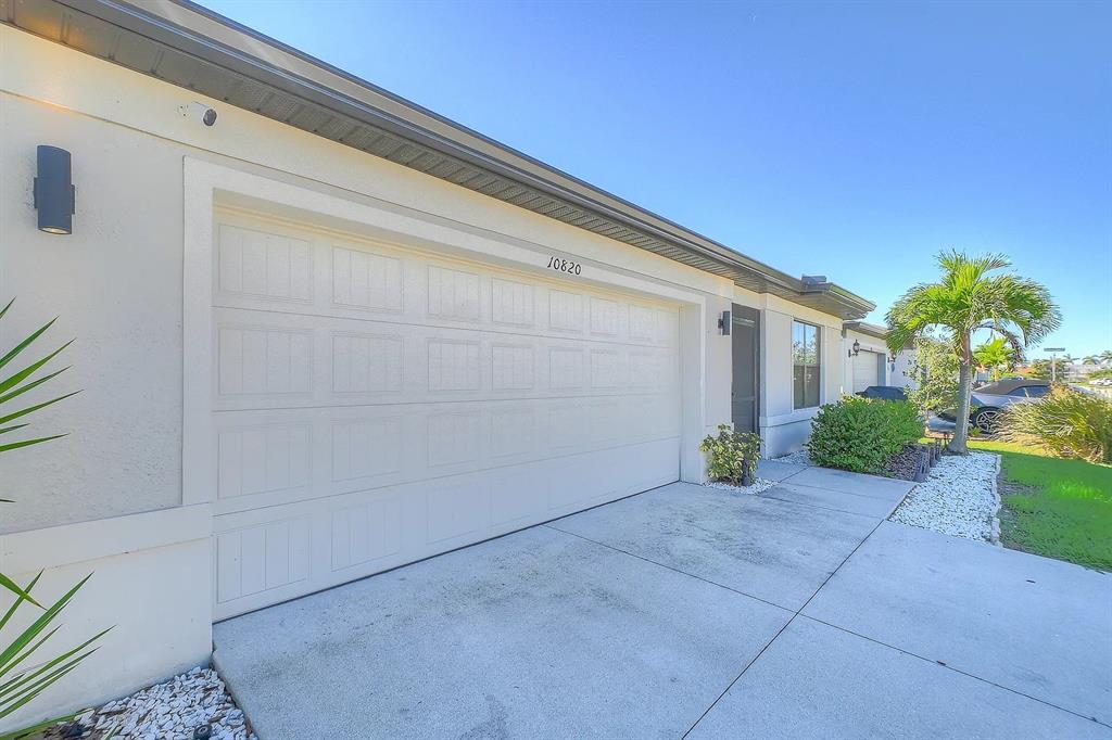 A beige house exterior features a white garage door, a concrete driveway, and landscaping — 10820 MARLBERRY WAY, NORTH FORT MYERS, FL