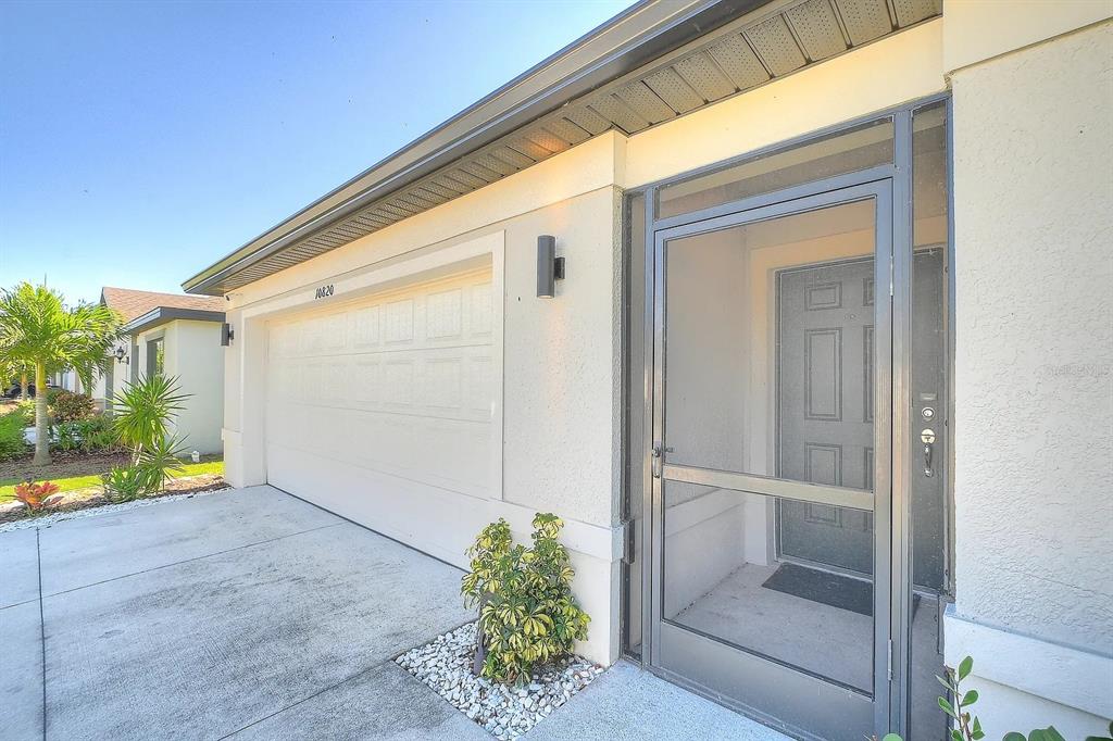 A beige house exterior features a two-car garage, a screen door, and a small plant — 10820 MARLBERRY WAY, NORTH FORT MYERS, FL