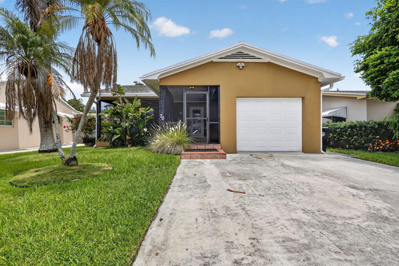 A tan single-story house features a screened front porch, a white garage door, and palm trees — 70 18th Avenue S, FL 33460, FL