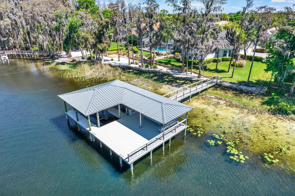 An aerial view of a boat dock with a metal roof extending into a lake — 5643 WHITE IBIS LANE, LAND O LAKES, FL