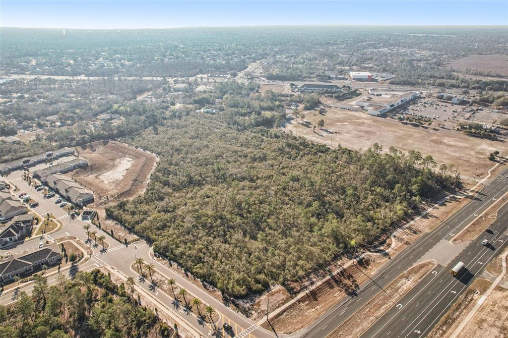 An aerial view shows a wooded vacant lot bordered by a road and residential development — 6414 COMMERCIAL WAY, WEEKI WACHEE, FL