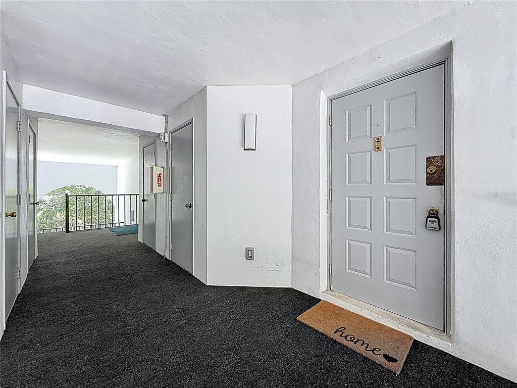 A gray front door with a welcome mat sits at the end of a hallway — 1372 PINE RIDGE CIRCLE E UNIT H3, TARPON SPRINGS, FL