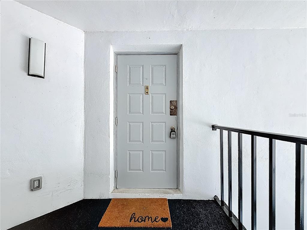 A light gray front door with a doormat sits on a balcony with railings — 1372 PINE RIDGE CIRCLE E UNIT H3, TARPON SPRINGS, FL
