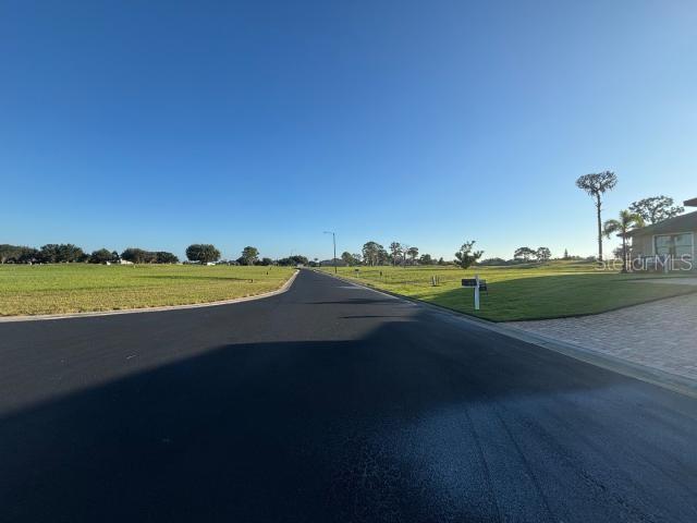 A paved road leads through a residential neighborhood with open grassy lots and clear skies — 4460 TOUSSANT DRIVE, AVON PARK, FL