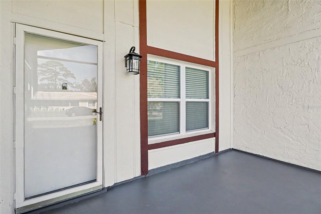 A white exterior wall with a glass door, a window, and a dark porch floor — 10157 BLUFF COURT, ORLANDO, FL