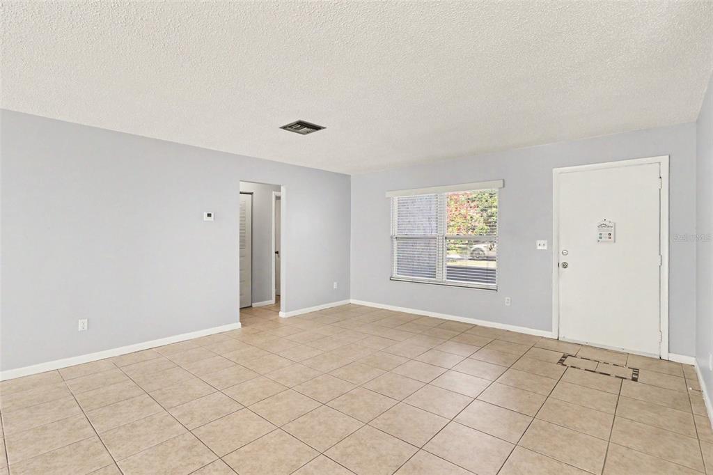 An empty living room features light gray walls, beige tile flooring, and a white front door — 10157 BLUFF COURT, ORLANDO, FL