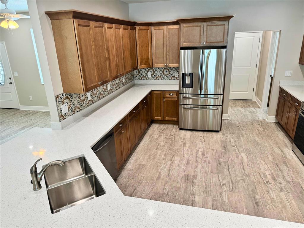 A kitchen features wood cabinets, white quartz countertops, stainless steel appliances, and patterned tile backsplash — 37549 TERI COURT, DADE CITY, FL