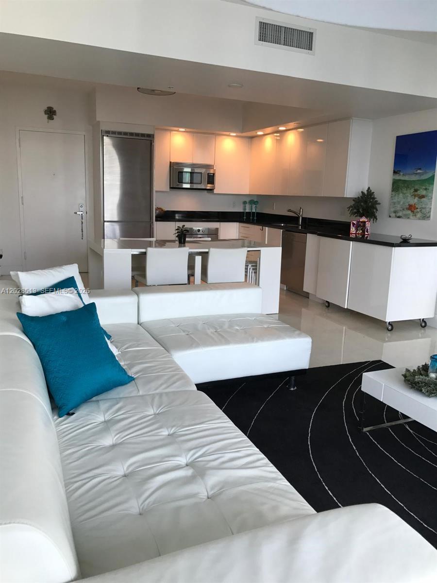A modern kitchen with white cabinetry and black countertops opens into a living room area — 92 SW 3rd St # 3712, Miami FL 33130, MIAMI, FL