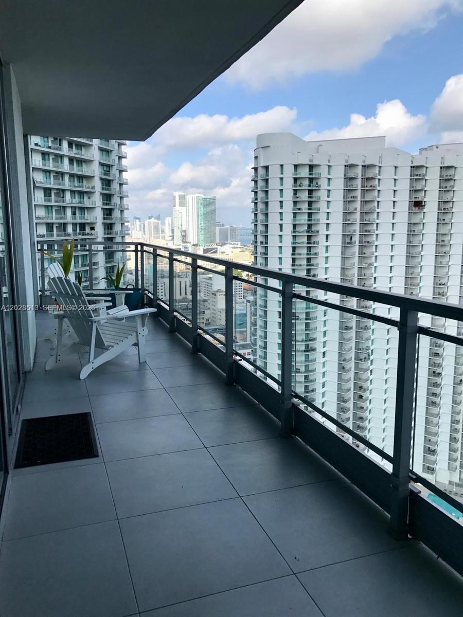 A high-rise balcony features gray tile flooring, a white chair, and views of city buildings — 92 SW 3rd St # 3712, Miami FL 33130, MIAMI, FL
