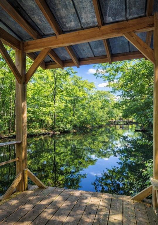 A wooden deck with a roof overlooks a calm, tree-lined pond on a sunny day — 12811 E BIG BUCK TRAIL, FLORAL CITY, FL