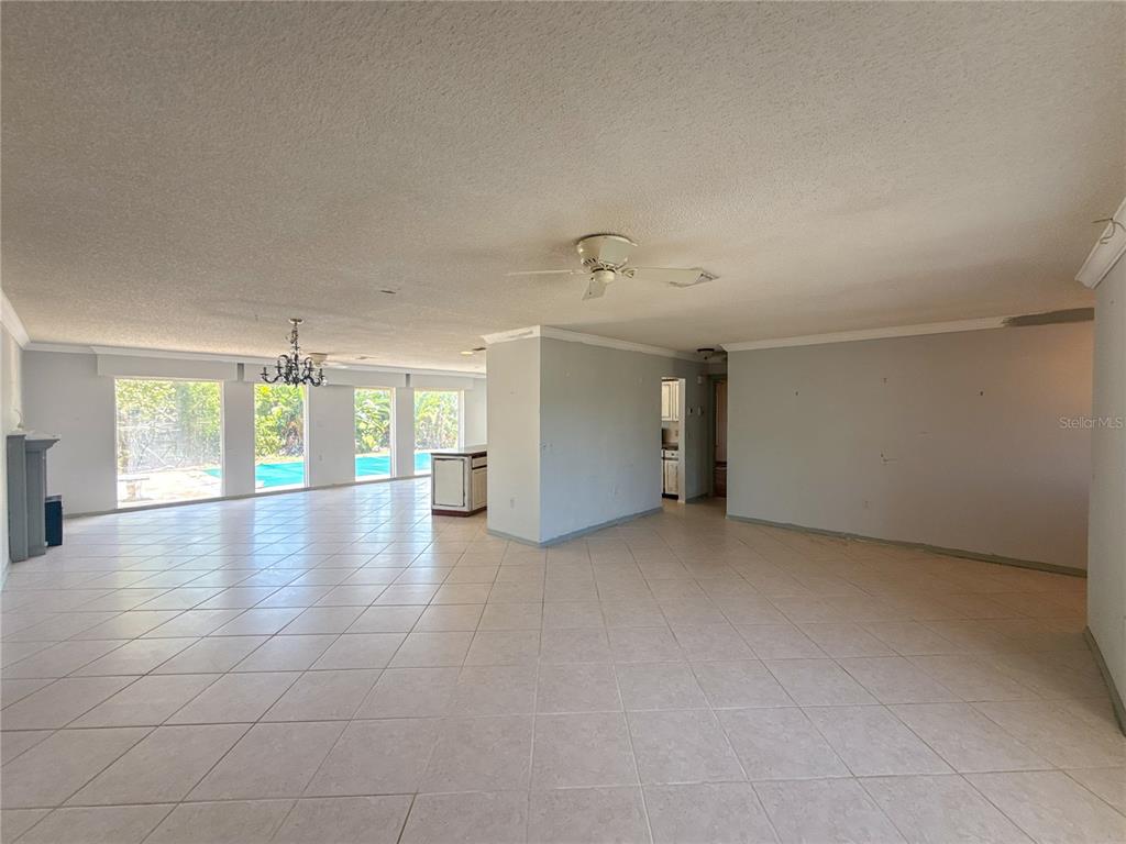 A spacious, open-concept living area features light-colored tile flooring, a ceiling fan, and large windows — 132 MARK TWAIN LANE, ROTONDA WEST, FL
