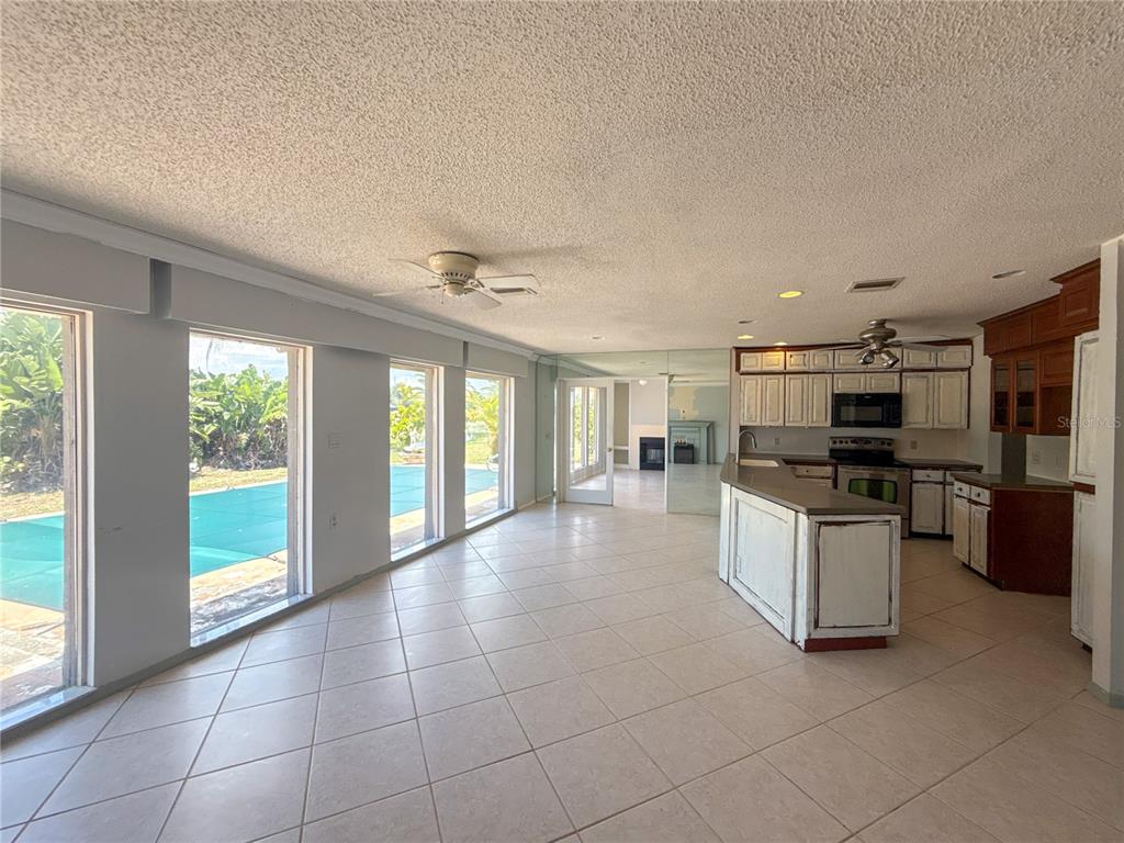 An open-concept kitchen and living area features tile floors, a kitchen island, and pool views — 132 MARK TWAIN LANE, ROTONDA WEST, FL