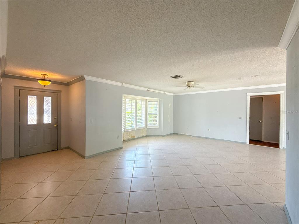 An empty living room features light-colored tile flooring, gray walls, and a bay window — 132 MARK TWAIN LANE, ROTONDA WEST, FL