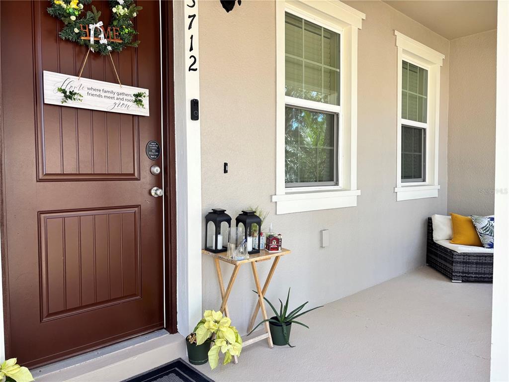 A covered front porch features a brown door, two windows, a small table, and seating — 13712 SUMMERPORT VILLAGE PARKWAY, WINDERMERE, FL