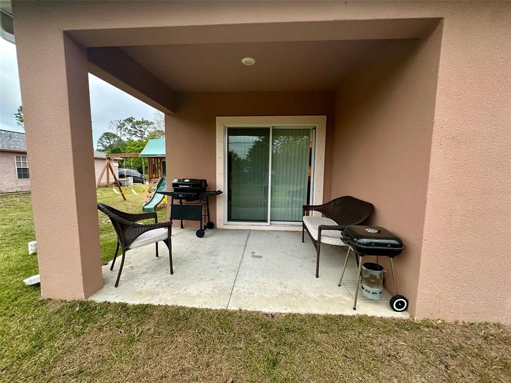 A covered concrete patio features two wicker chairs and two charcoal grills — 538 VIN ROSE CIRCLE SE, PALM BAY, FL