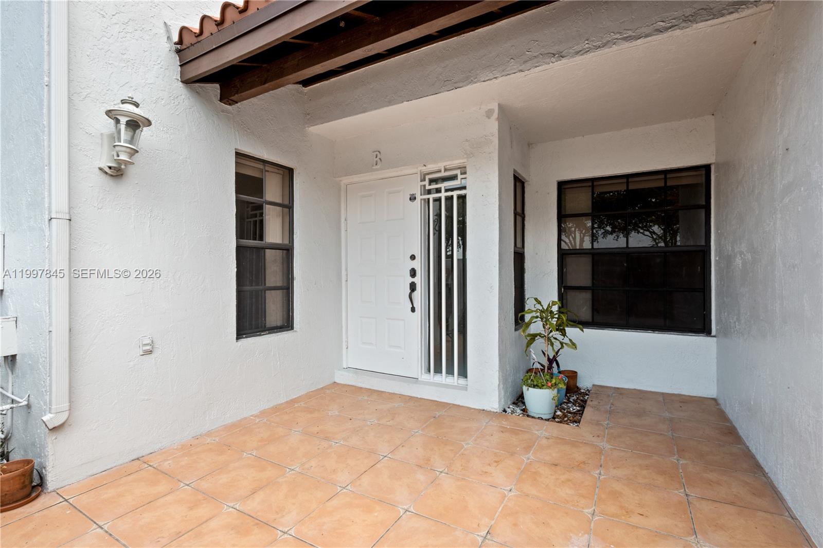A white front door with a side window sits on a tiled patio entrance — 6211 SW 138th Ct # B, Miami FL 33183, MIAMI, FL