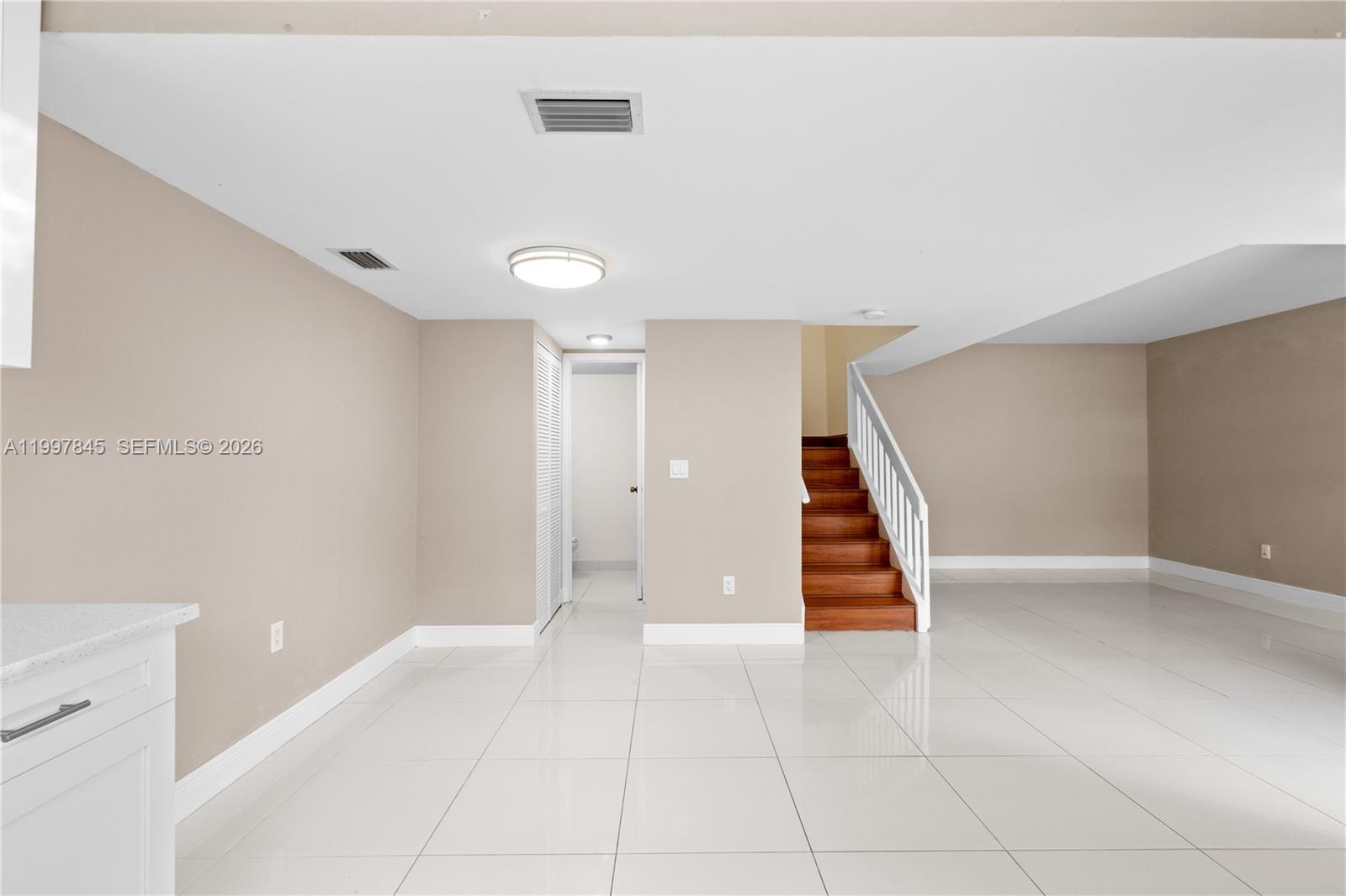 A room with white tile floors, beige walls, and a wooden staircase with a white railing — 6211 SW 138th Ct # B, Miami FL 33183, MIAMI, FL