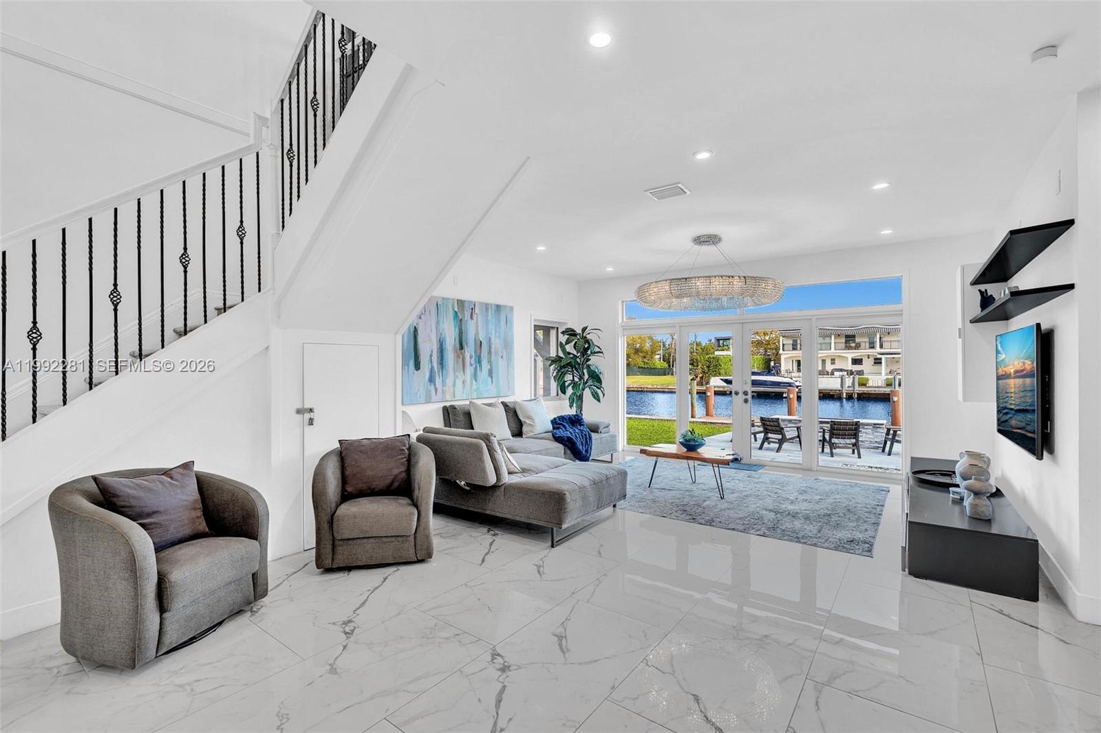 A modern living room features marble floors, a staircase, and glass doors overlooking a canal — 472 Sunset Dr, Hallandale Beach FL 33009, HALLANDALE BEACH, FL