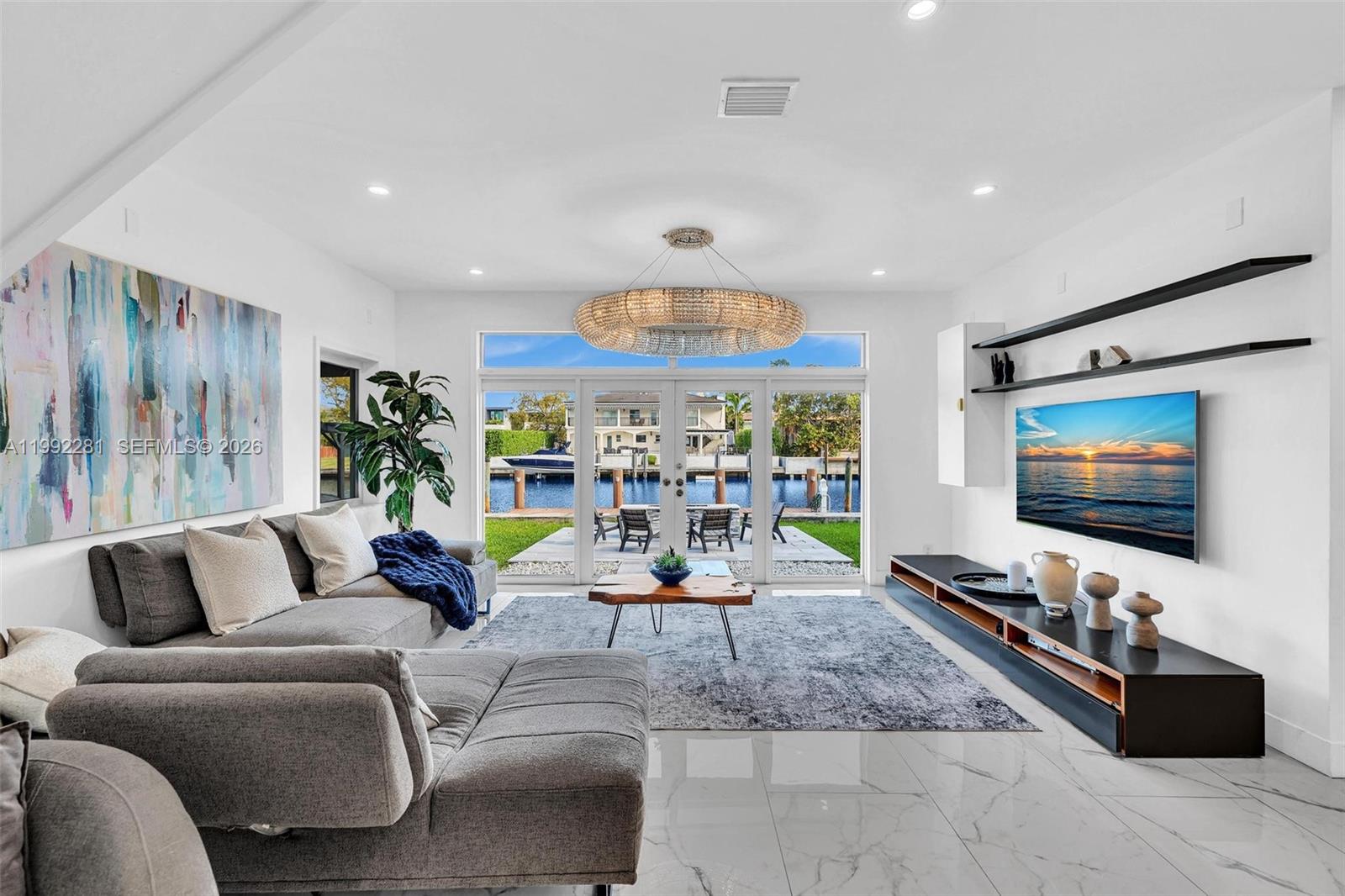 A modern living room features a large sectional sofa, a crystal chandelier, and waterfront views — 472 Sunset Dr, Hallandale Beach FL 33009, HALLANDALE BEACH, FL